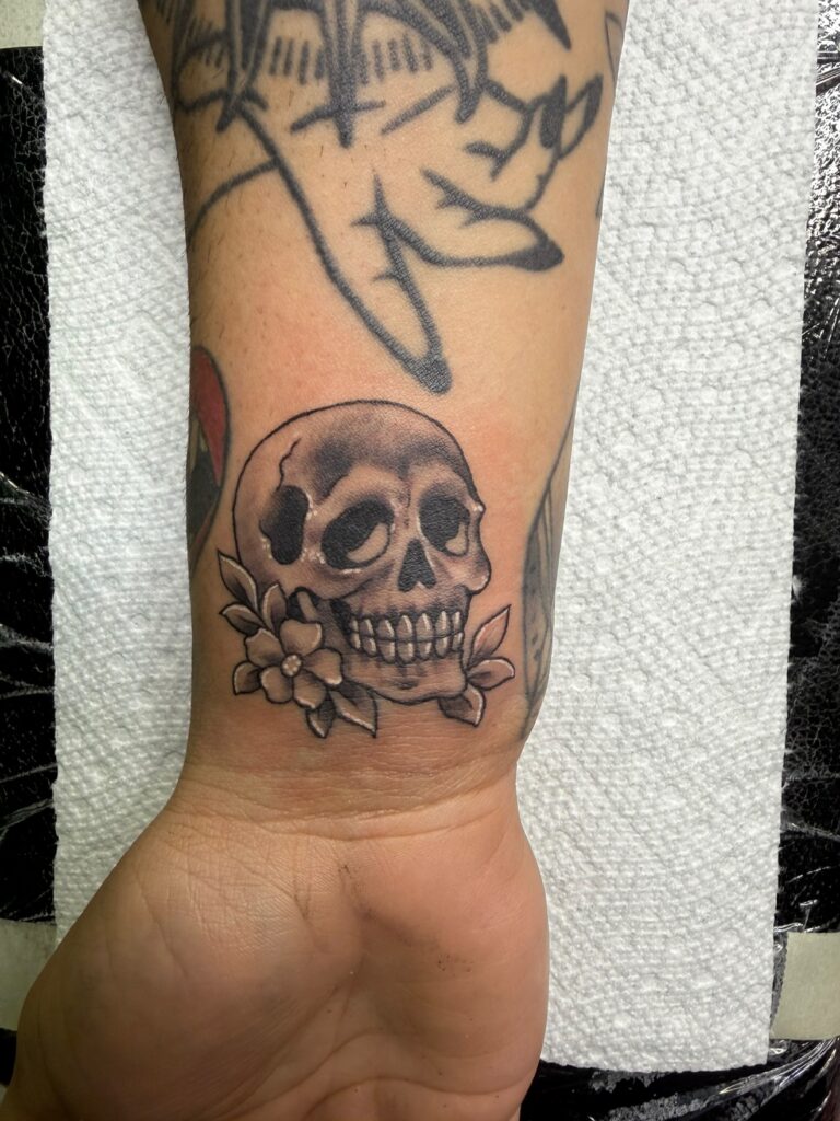 Black-and-gray skull and flower tattoo at a client's wrist at Off Grid Tattoo in Ellijay GA